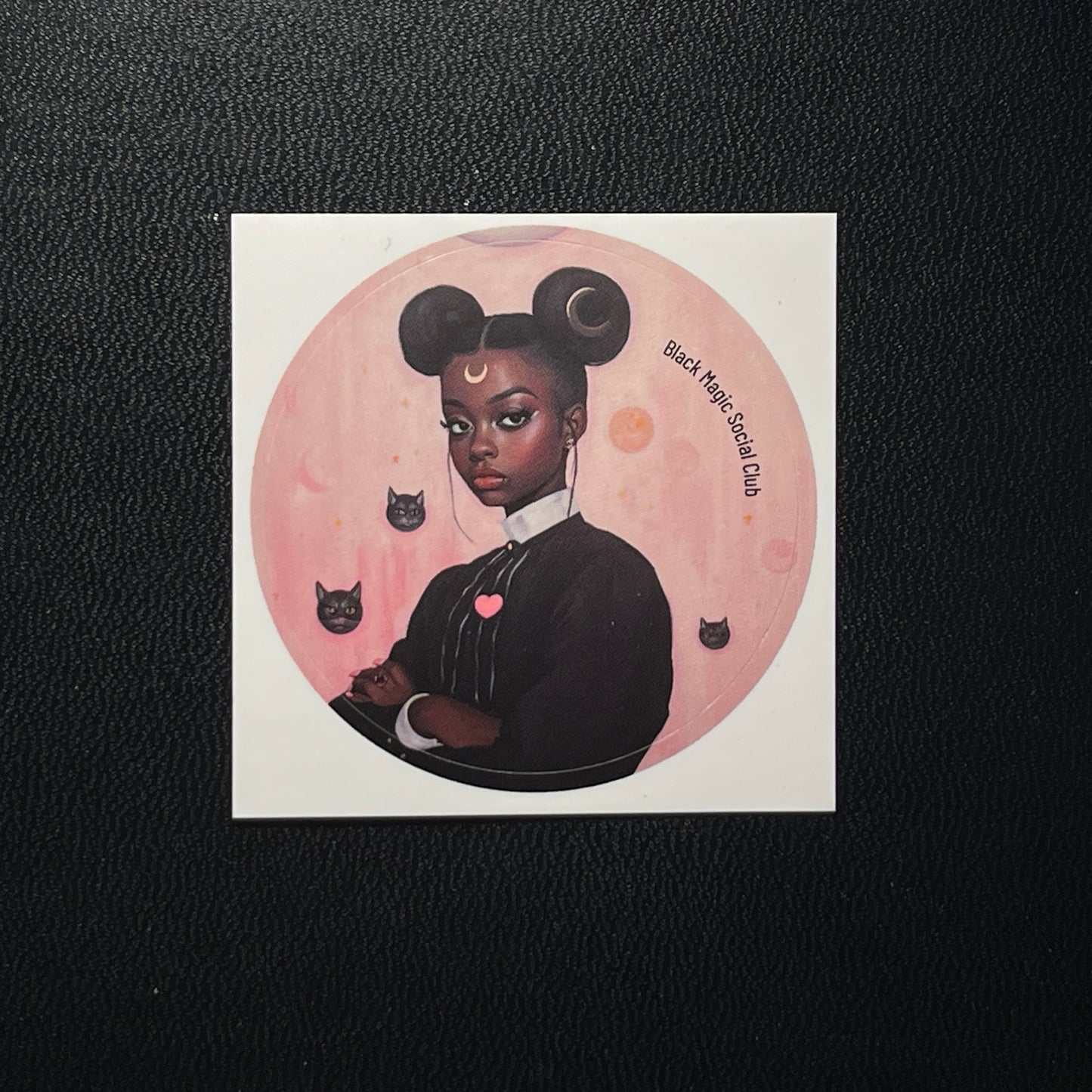 Sticker of a stylized illustration of a woman with black hair bun, surrounded by cats and a pink moon on a black background.